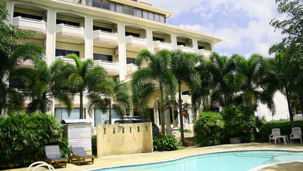 Un hôtel doté d’une piscine, de palmiers et de chaises longues.