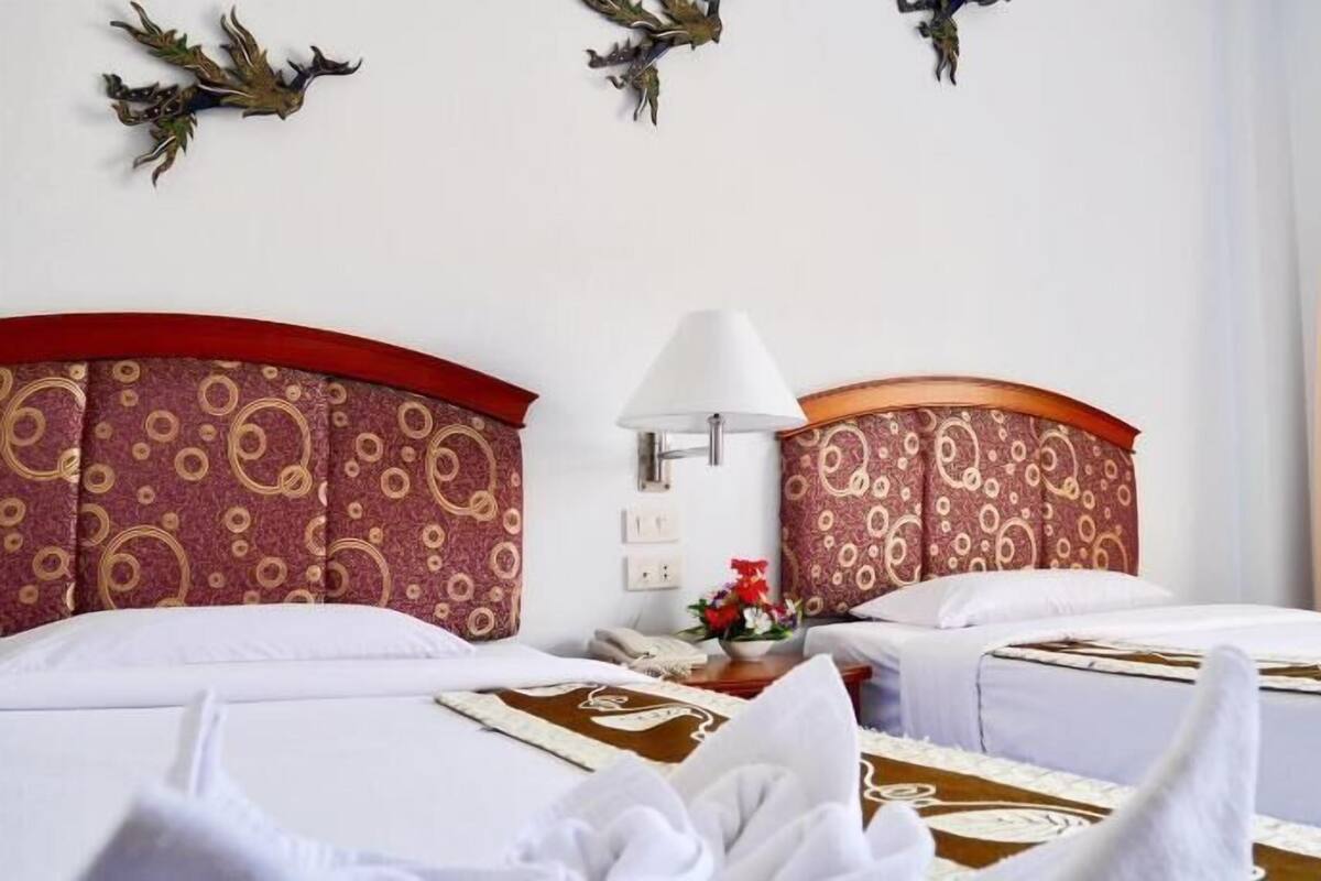Een hotelkamer met twee bedden, een nachtkastje, een lamp, decoratieve wandkunst en een raam met gordijnen.