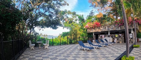 An outdoor patio with stone flooring, lounge chairs, and a stone wall with plants.
