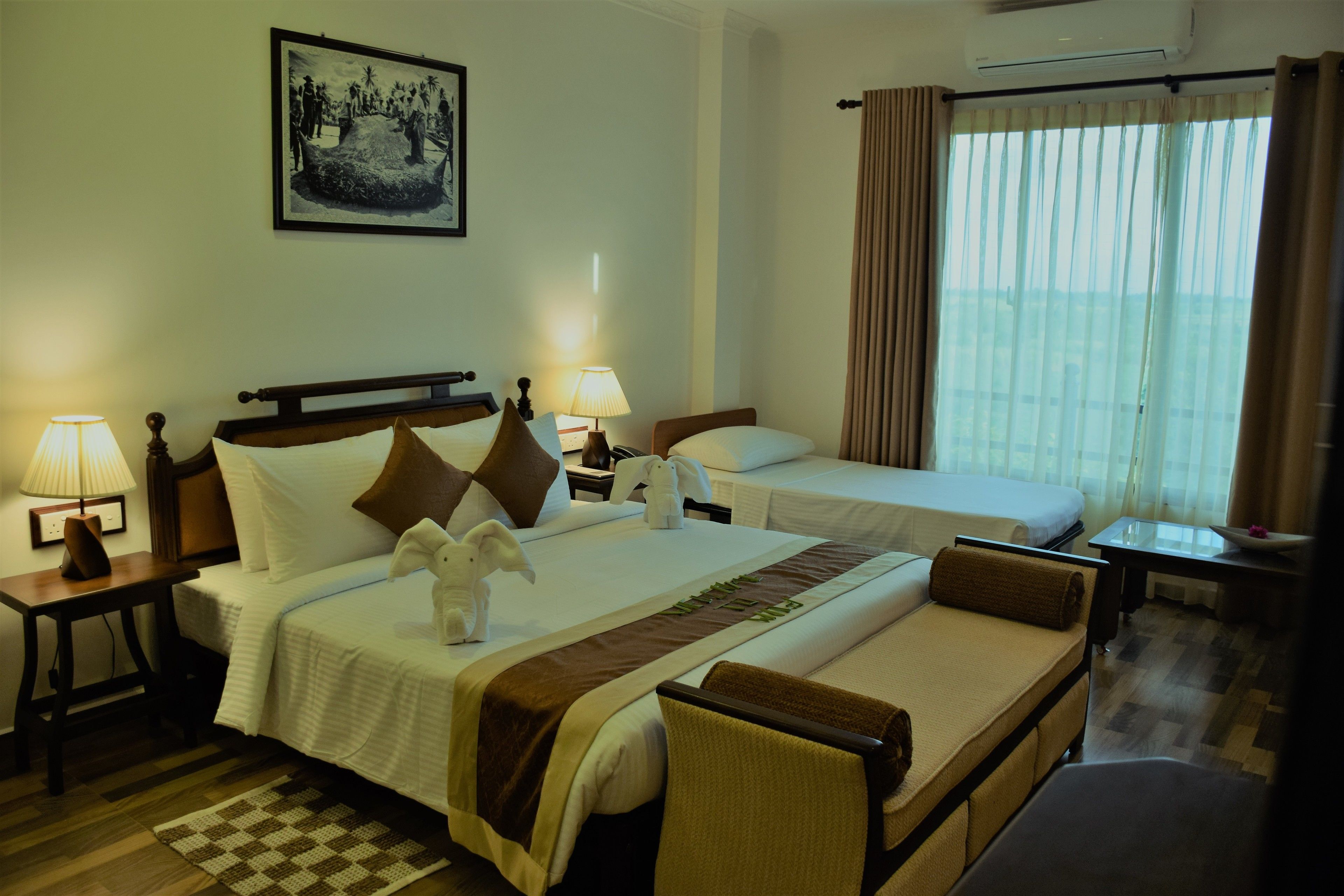 A hotel room with two beds, a checkered rug, a framed picture on the wall, and a window with curtains.