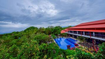 A hotel with a swimming pool surrounded by lush greenery and a red-roofed building.