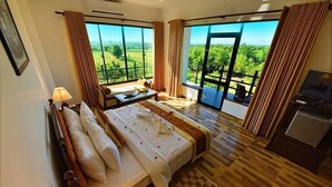 Een hotelkamer met een groot bed, een bureau, een stoel en uitzicht op het platteland door grote ramen.