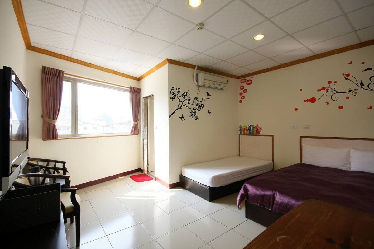 A hotel room with a bed, a desk, a chair, a TV, and a window with curtains.