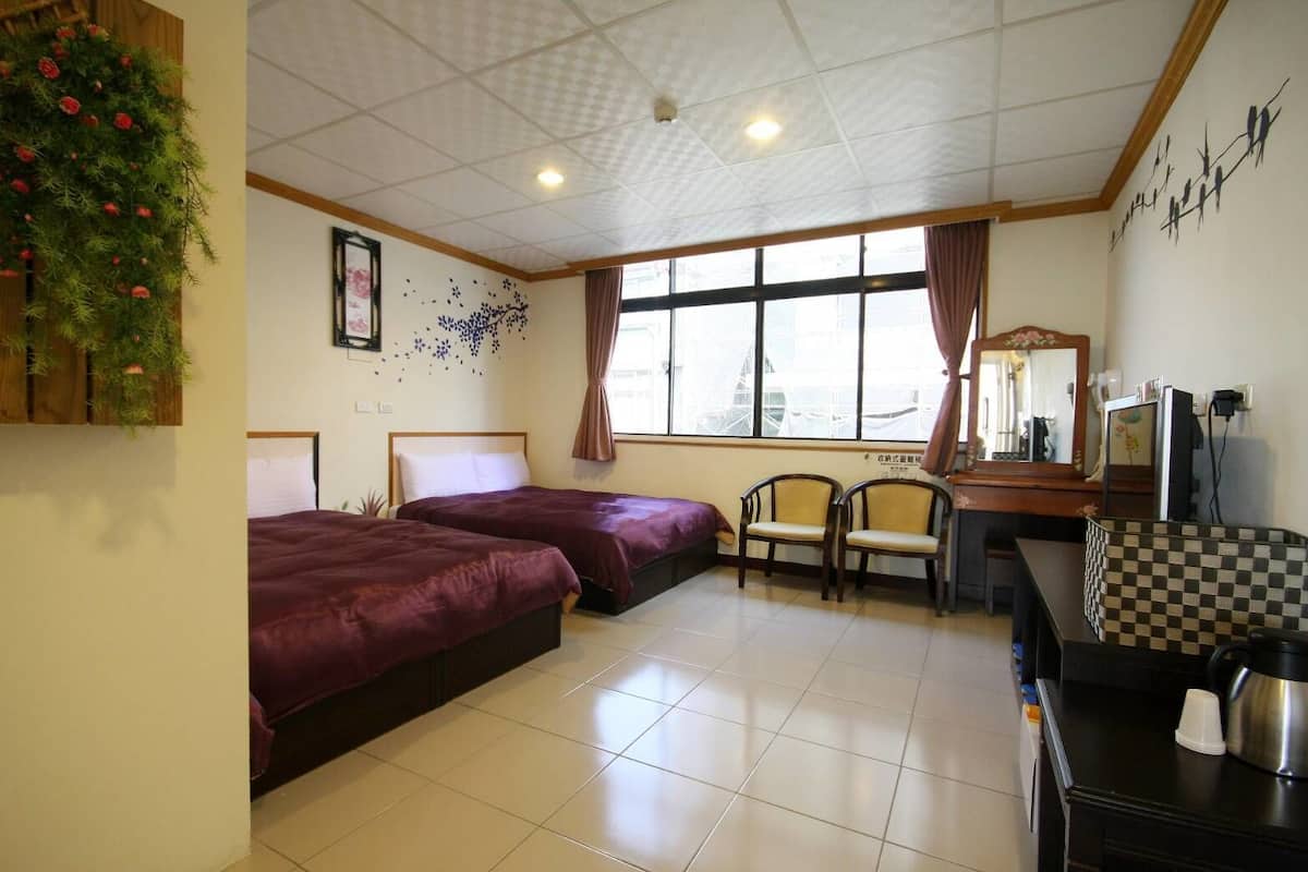 A hotel room with two beds, a desk, a chair, a window with curtains, a mirror, and a checkered tablecloth.