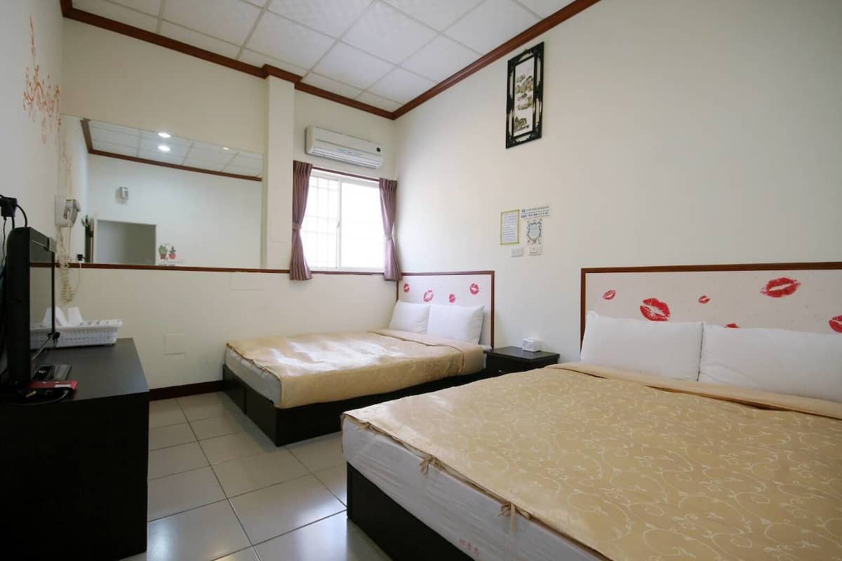 A hotel room with two beds, a desk with a telephone, and an air conditioning unit.