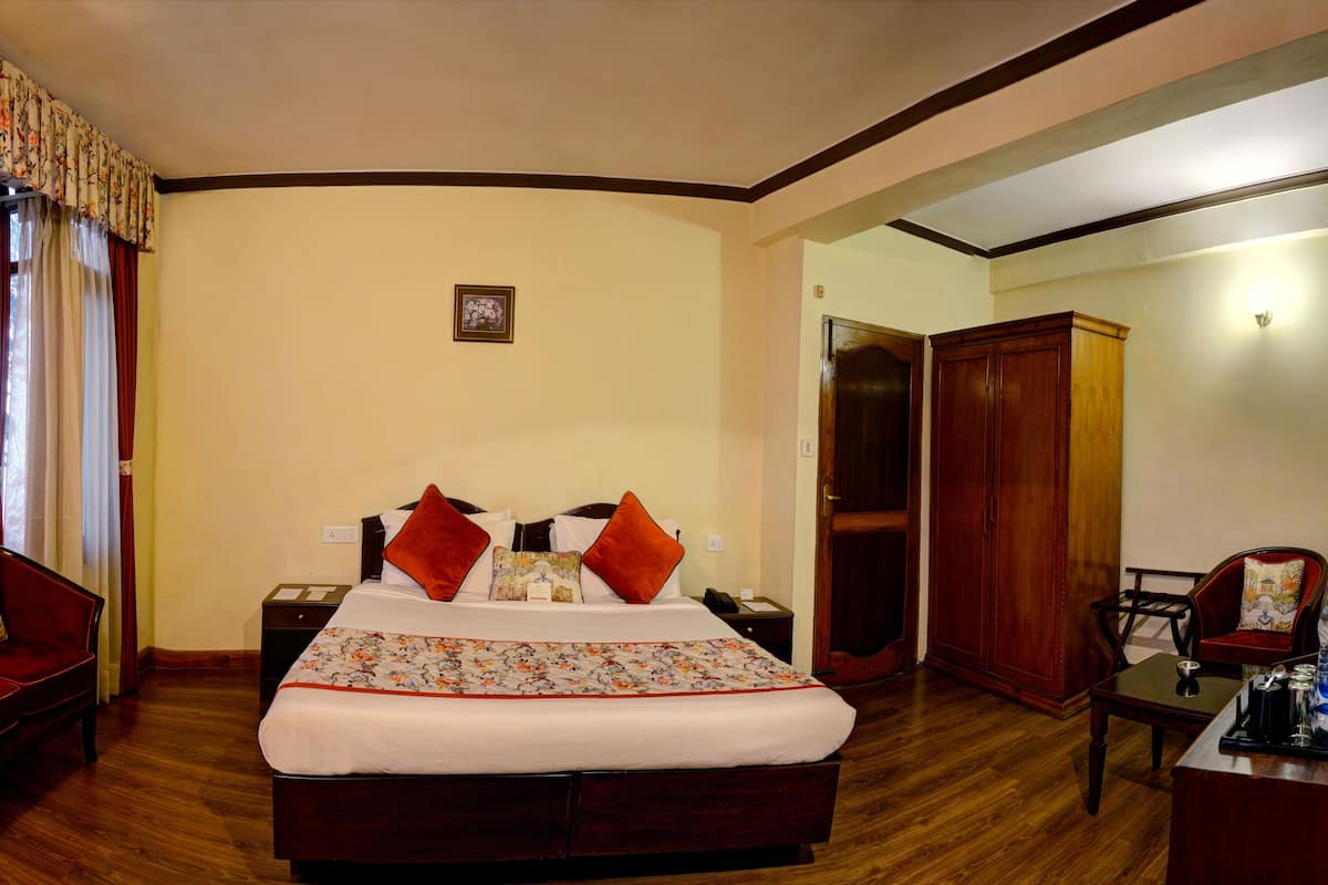 A hotel room with a large bed, a wooden nightstand, a desk with a chair, a red sofa, and a wardrobe.