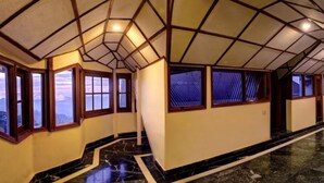 Un couloir d’hôtel doté d’un plafond au design géométrique, d’un sol en marbre et de grandes fenêtres offrant une vue panoramique.