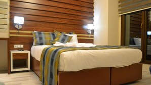A modern hotel room with a wooden headboard, a bed with a striped blanket, two bedside lamps, and a small bedside table. - Altinpark Hotel (Kayseri)