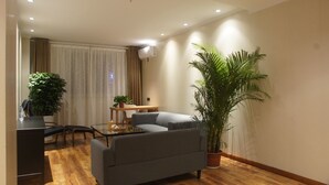A modern living room with a sofa, a dining table with chairs, and two potted plants. - Manchen Hotel (Xi'an)