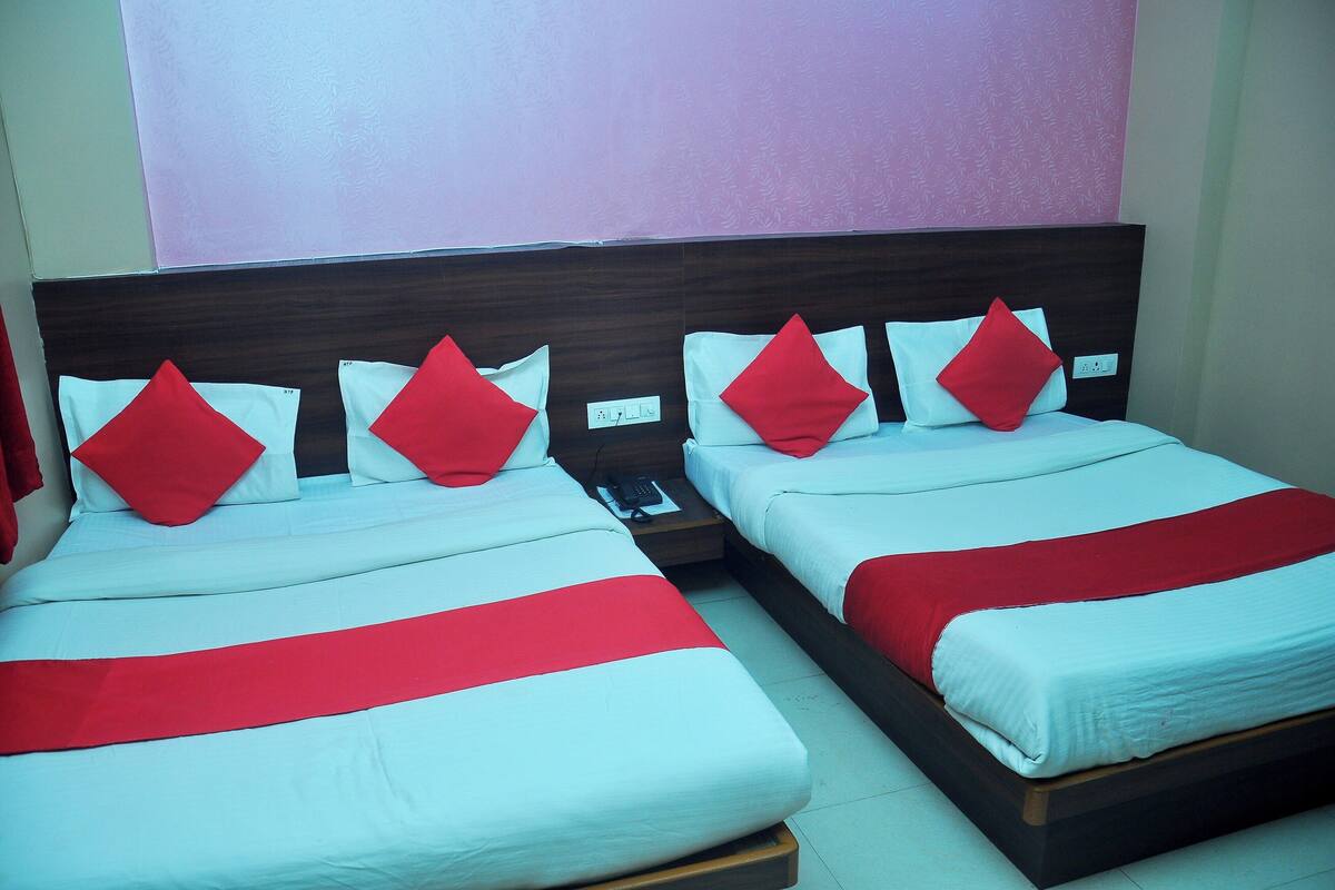 Dos camas con ropa de cama roja y blanca, un cabecero de madera y un enchufe en la pared.