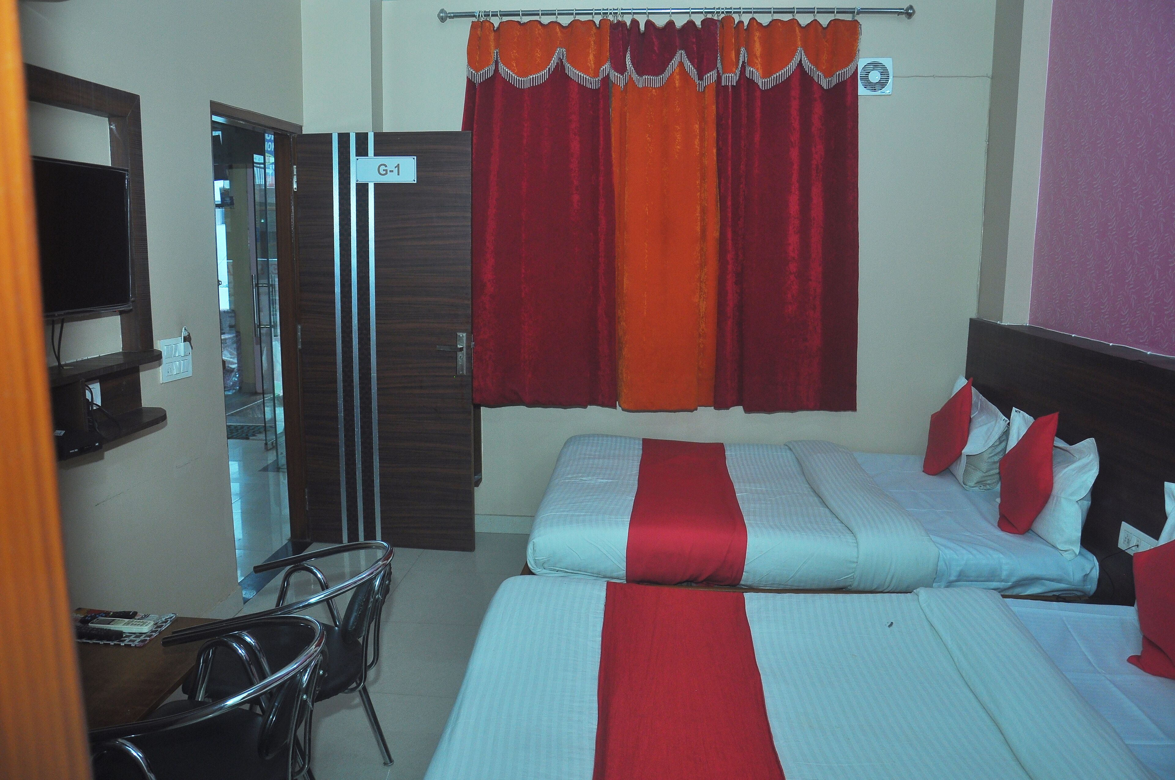 A hotel room with a bed, a TV, a desk with chairs, and a bathroom door.