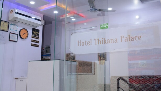 Un área de recepción con un separador de vidrio, un reloj y un letrero que dice "Hotel Thikana Palace".