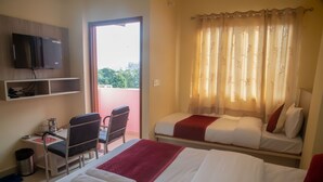 Habitación de hotel con dos camas, un escritorio con una silla, un televisor montado en la pared y un balcón con vistas a la ciudad.