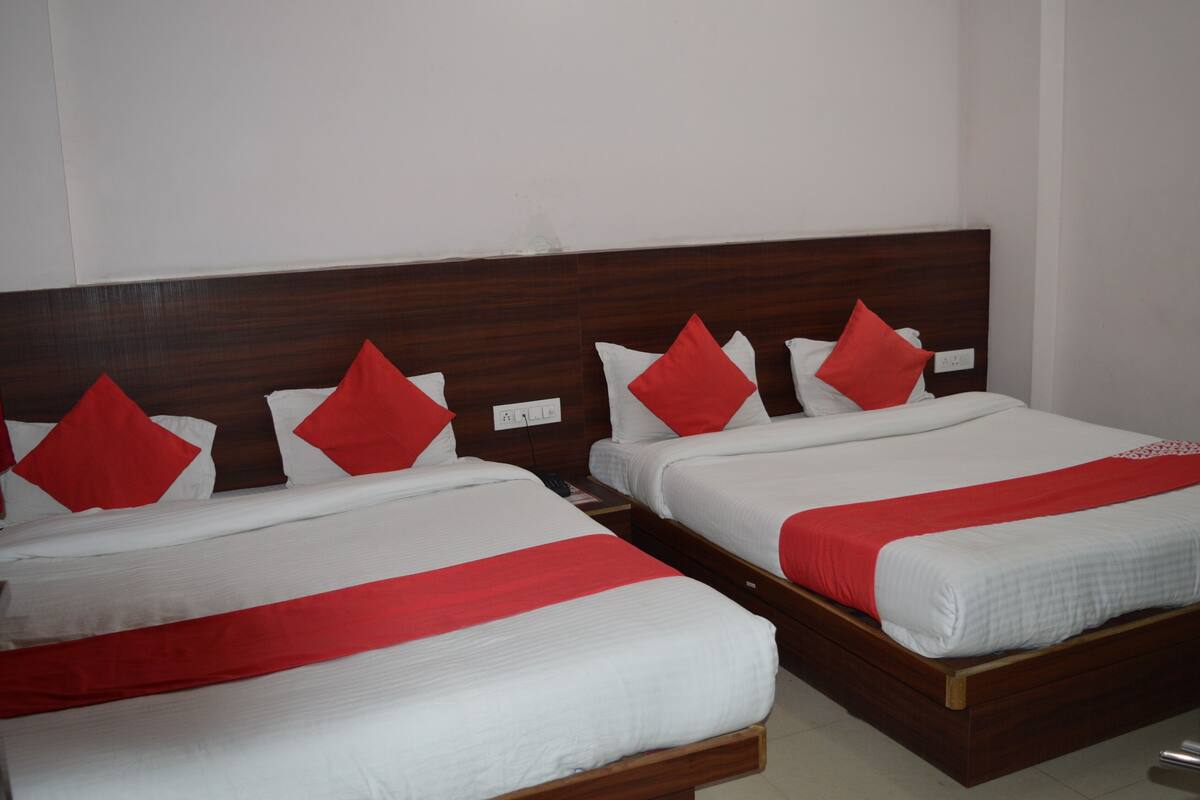Dos camas juntas con cabeceros de madera, ropa de cama blanca y almohadas rojas.