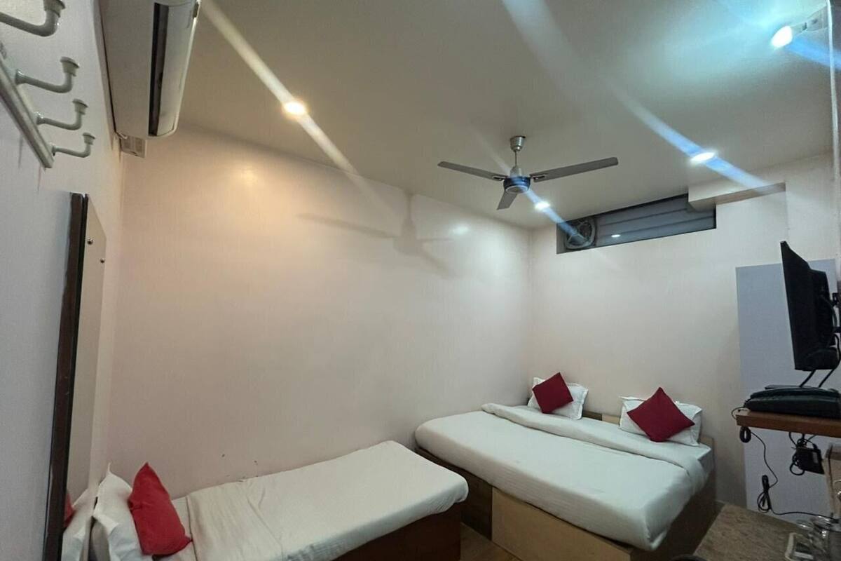 Una habitación pequeña y funcional con dos camas individuales, un ventilador de techo y una televisión.