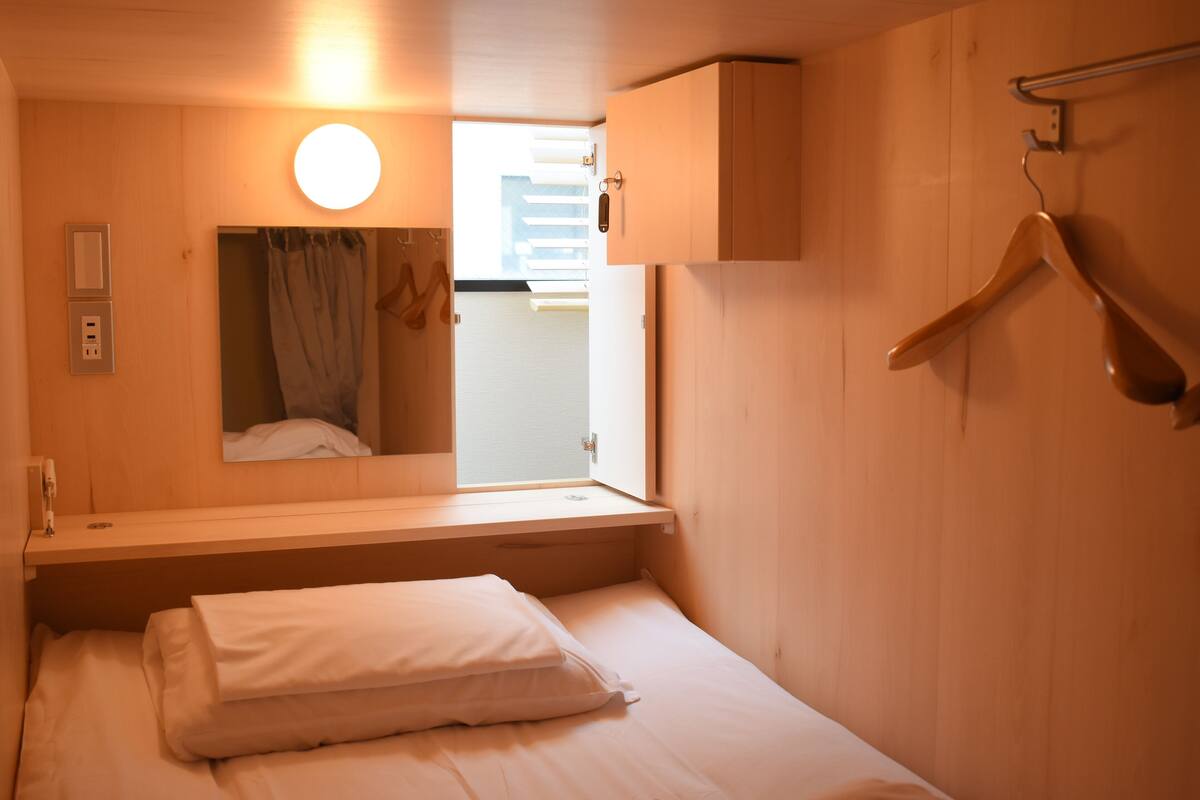 Un dormitorio con cama, mesita de noche, perchero y ventana con cortinas.