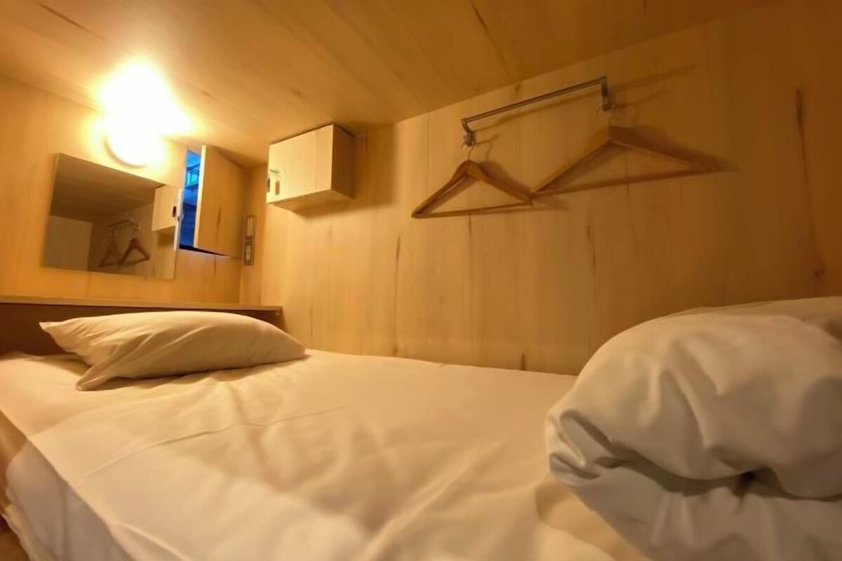 Habitació d'hotel amb un llit, una barra de roba penjant, un mirall i una làmpada.