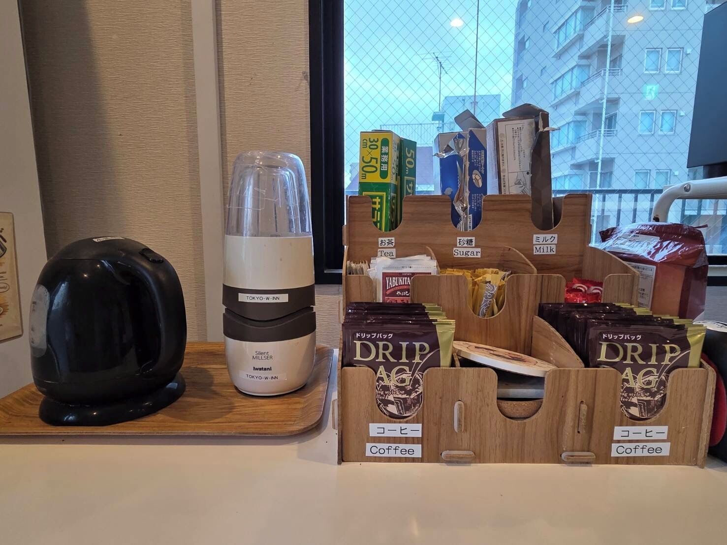 A coffee station with a coffee maker, a grinder, and labeled containers for coffee, tea, sugar, and milk.