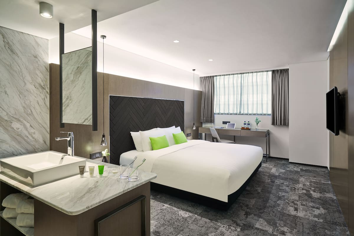 Une chambre d’hôtel moderne dotée d’un grand lit, d’un bureau, d’une salle de bain avec un meuble-lavabo en marbre et d’un grand miroir.