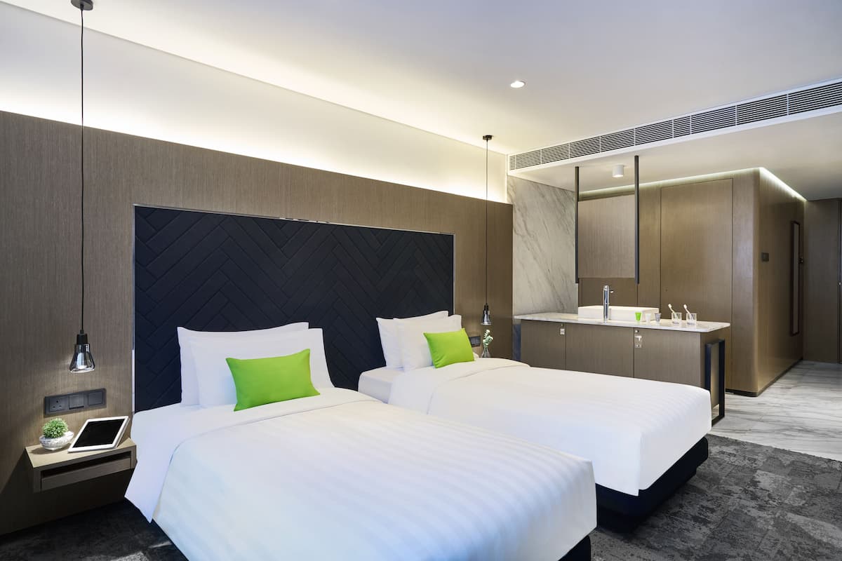 Une chambre d’hôtel moderne avec deux lits, un grand miroir, une coiffeuse intégrée et une petite table de chevet avec une lampe.