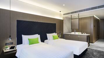 A modern hotel room with two beds, a large mirror, a built-in vanity, and a small bedside table with a lamp.