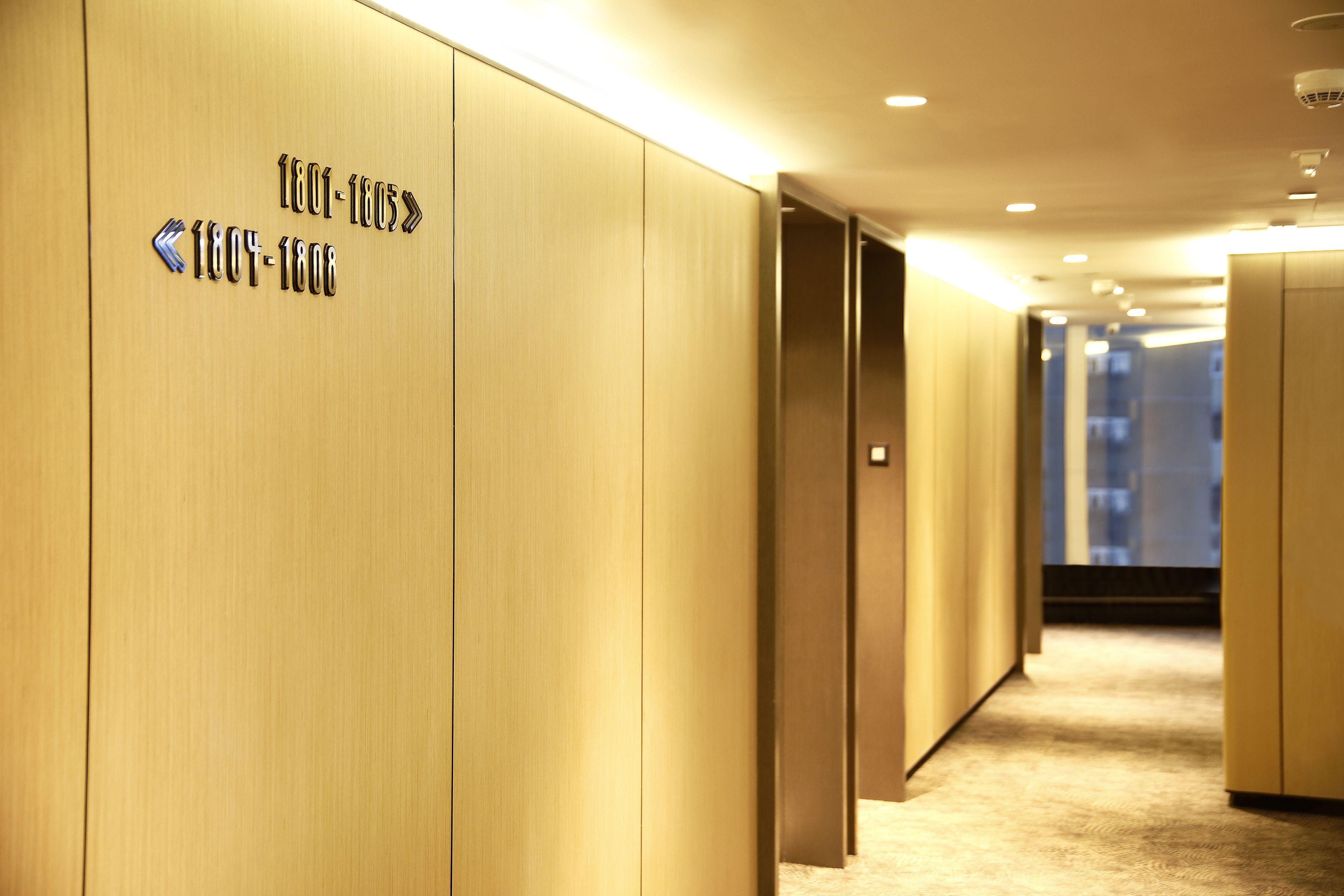 A hallway with wooden paneling and directional signs indicating room numbers.