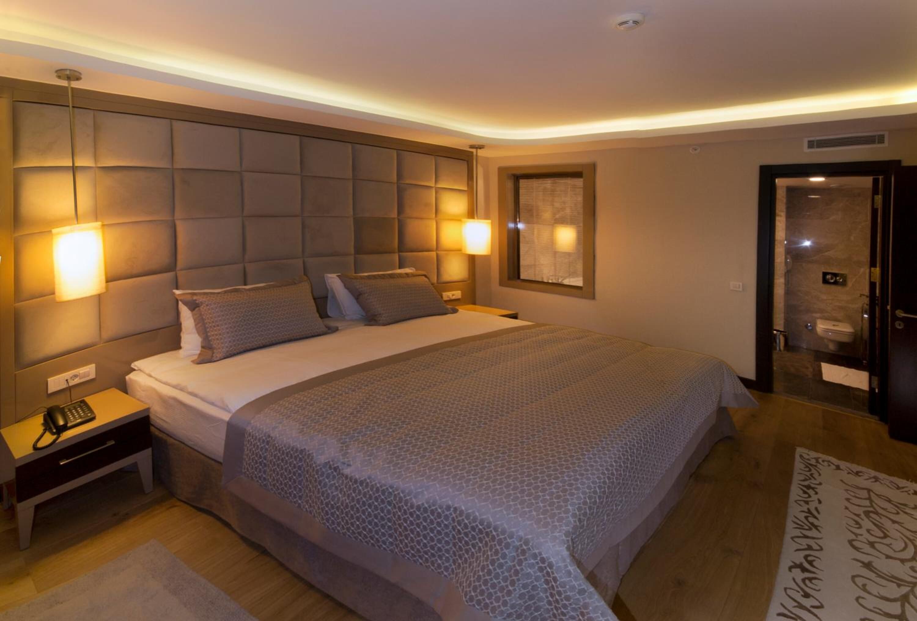 A modern hotel room with a large bed, a bedside table with a phone, and a wall-mounted light fixture.