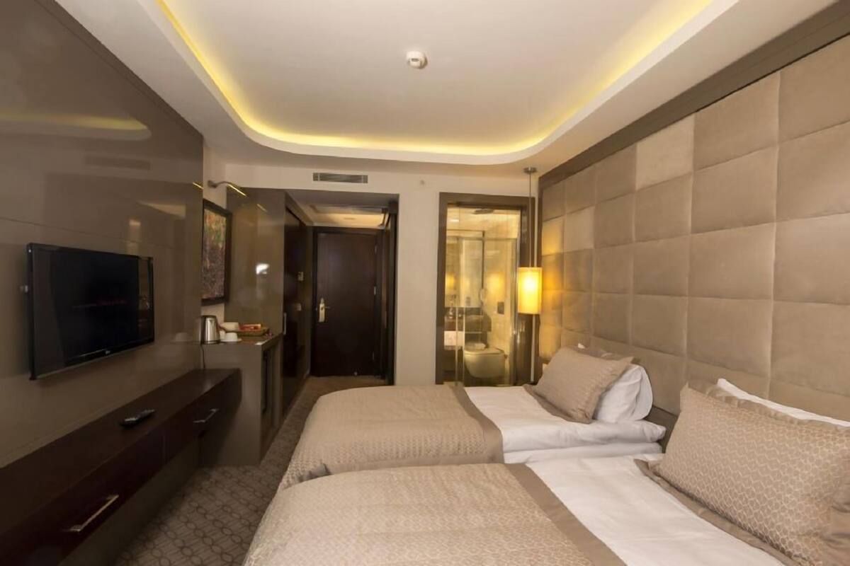 Ein Hotelzimmer mit zwei Betten, einem Fernseher, einem Schreibtisch und einem durchgehenden Türspalt sichtbaren Badezimmer.