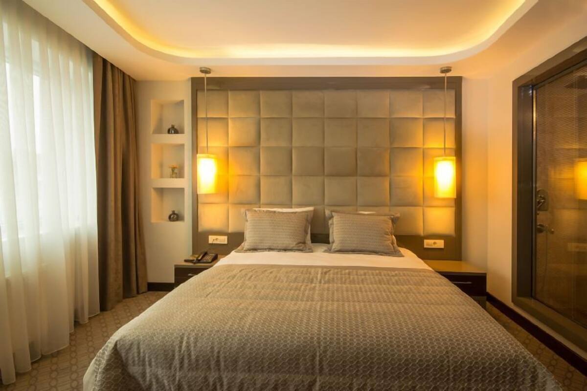Ein Hotelzimmer mit einem großen Bett, zwei Nachttischen, einer Kopfteilbeleuchtung, einem Kleiderschrank und einem Vorhangfenster.