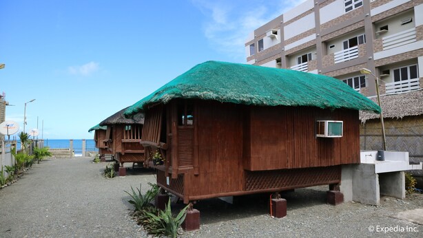 A wooden house with a thatched roof, situated on a gravel path with a view of the sea. - Nipa Hut Villa by AMCO Extension (Baler)
