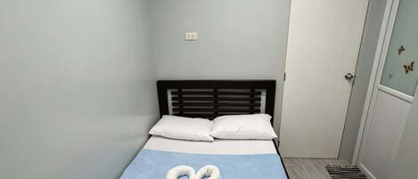 A small, single-bed room with a sloped ceiling, a white door with a window, and a blue bedspread with a swan design.