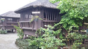 A traditional wooden structure with a thatched roof, labeled "KUBO A," surrounded by lush greenery and potted plants. - Nipa Hut Villa by AMCO Extension (Baler)
