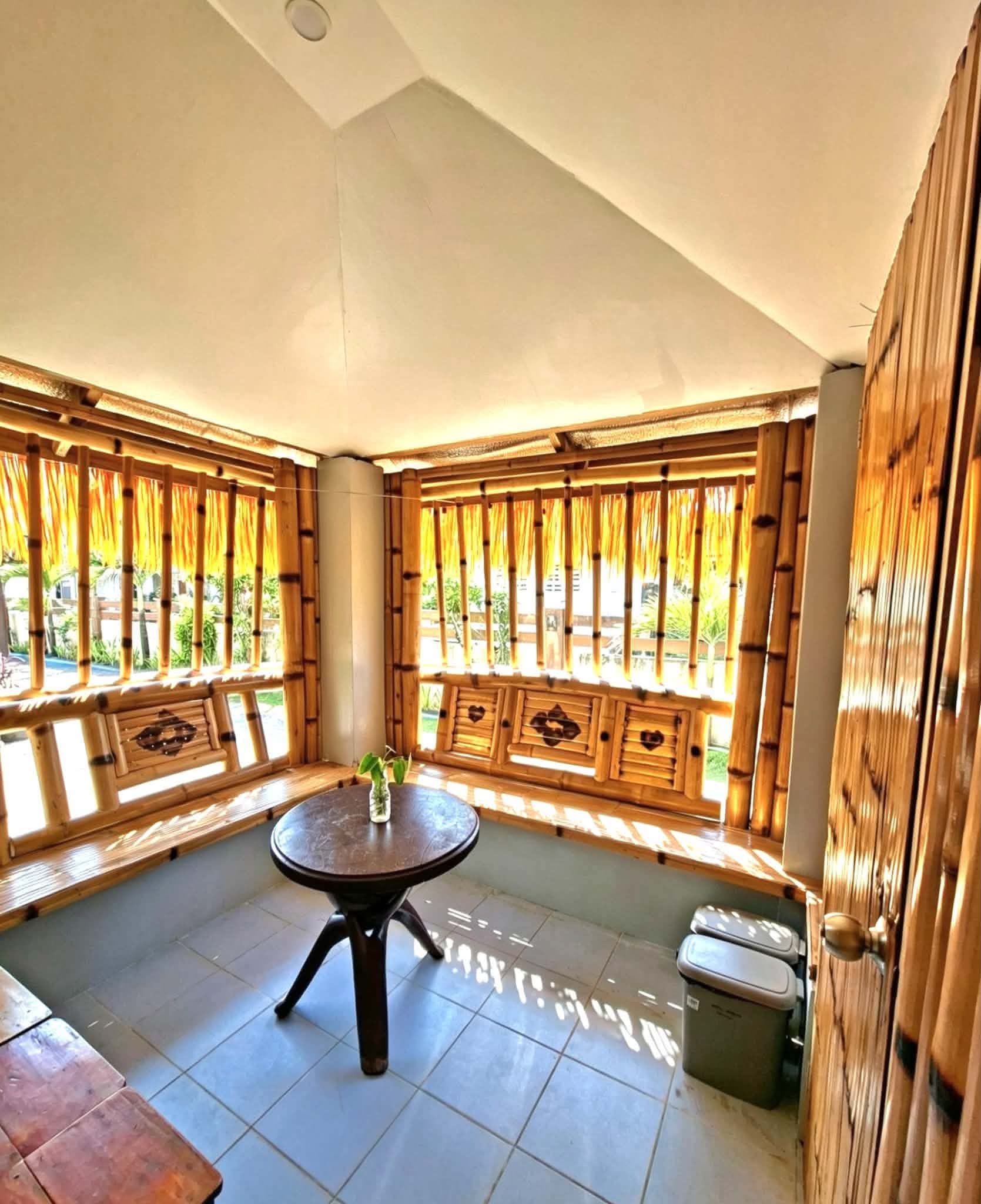 A room with a round table, bamboo window frames, and a view of greenery outside.