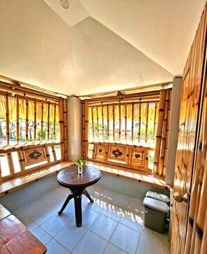 A room with a round table, bamboo window frames, and a view of greenery outside. - AMCO BEACH RESORT EXTENSION (Baler)
