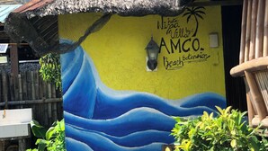 A building with a mural of waves and a palm tree, labeled "Nipapa by AMCO Beach Extension." - Nipa Hut Villa by AMCO Extension (Baler)