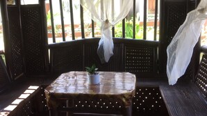 A covered outdoor seating area with a table and bench, a potted plant, and a view of greenery outside. - Nipa Hut Villa by AMCO Extension (Baler)