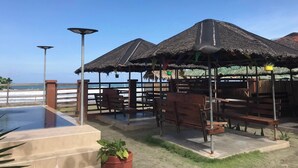 A beachside restaurant with thatched-roof outdoor seating and a pool. - Nipa Hut Villa by AMCO Extension (Baler)