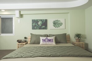 A neatly arranged bedroom with a bed, a pillow with text, a wall with leaf art, and a small plant on a nightstand. - The Homee Cozy Modern Studio Apartment (Ho Chi Minh City)