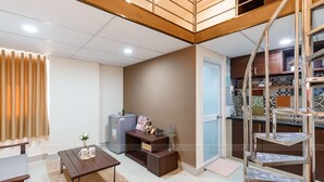 A modern living room with a wooden ceiling, a small dining table, a sofa, and a staircase with a metal railing. - The Homee Cozy Modern Studio Apartment (Ho Chi Minh City)