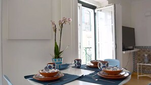 A dining area with a round table set for four, blue and orange patterned tableware, a potted orchid, and a view of the outdoors through a glass door. - Chiado Blue by Homing (Lisbon)