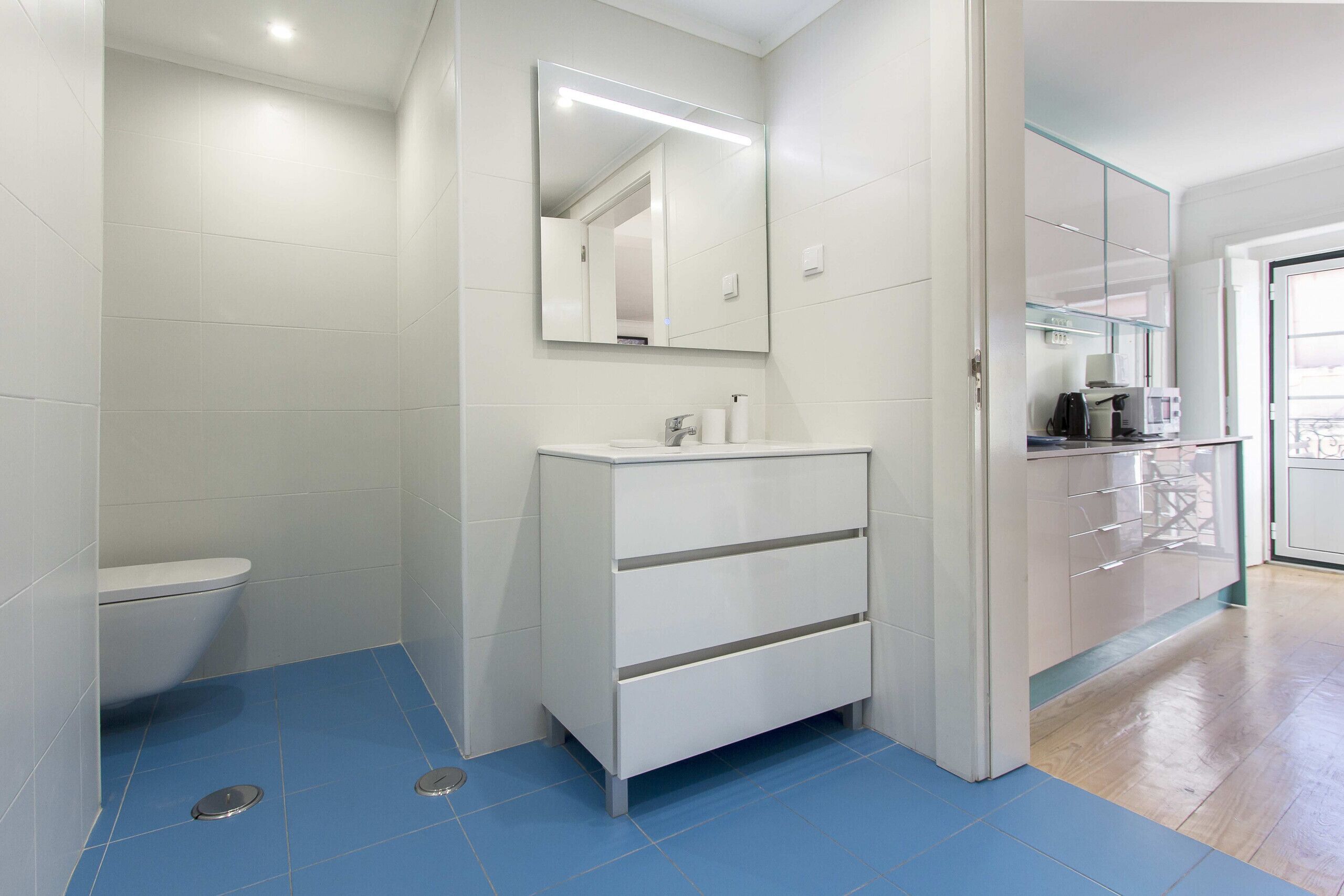 Un baño moderno con un inodoro blanco, un lavabo blanco con un espejo encima y un suelo azul.
