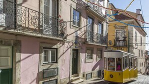 A yellow tram on a cobblestone street, passing by a pink building with balconies and a green door. - Chiado Blue by Homing (Lisbon)