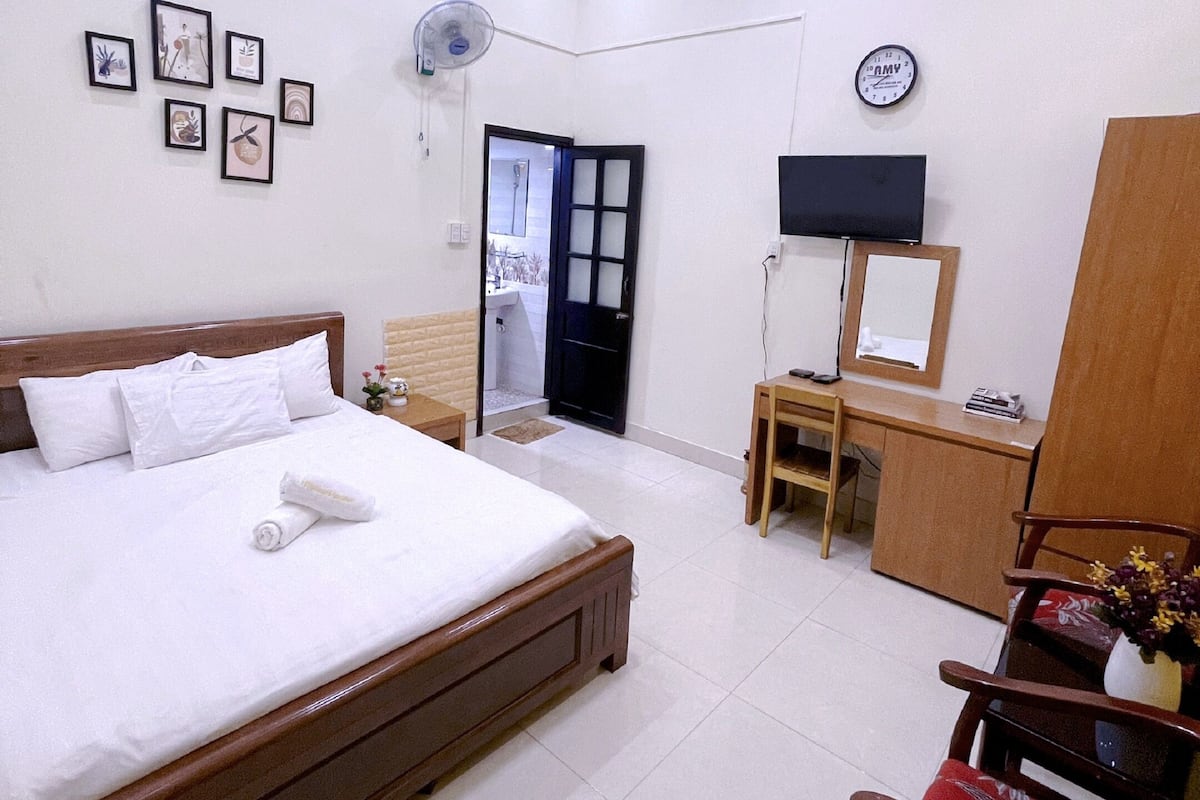 A hotel room with a bed, a desk, a chair, a TV, and a clock on the wall.