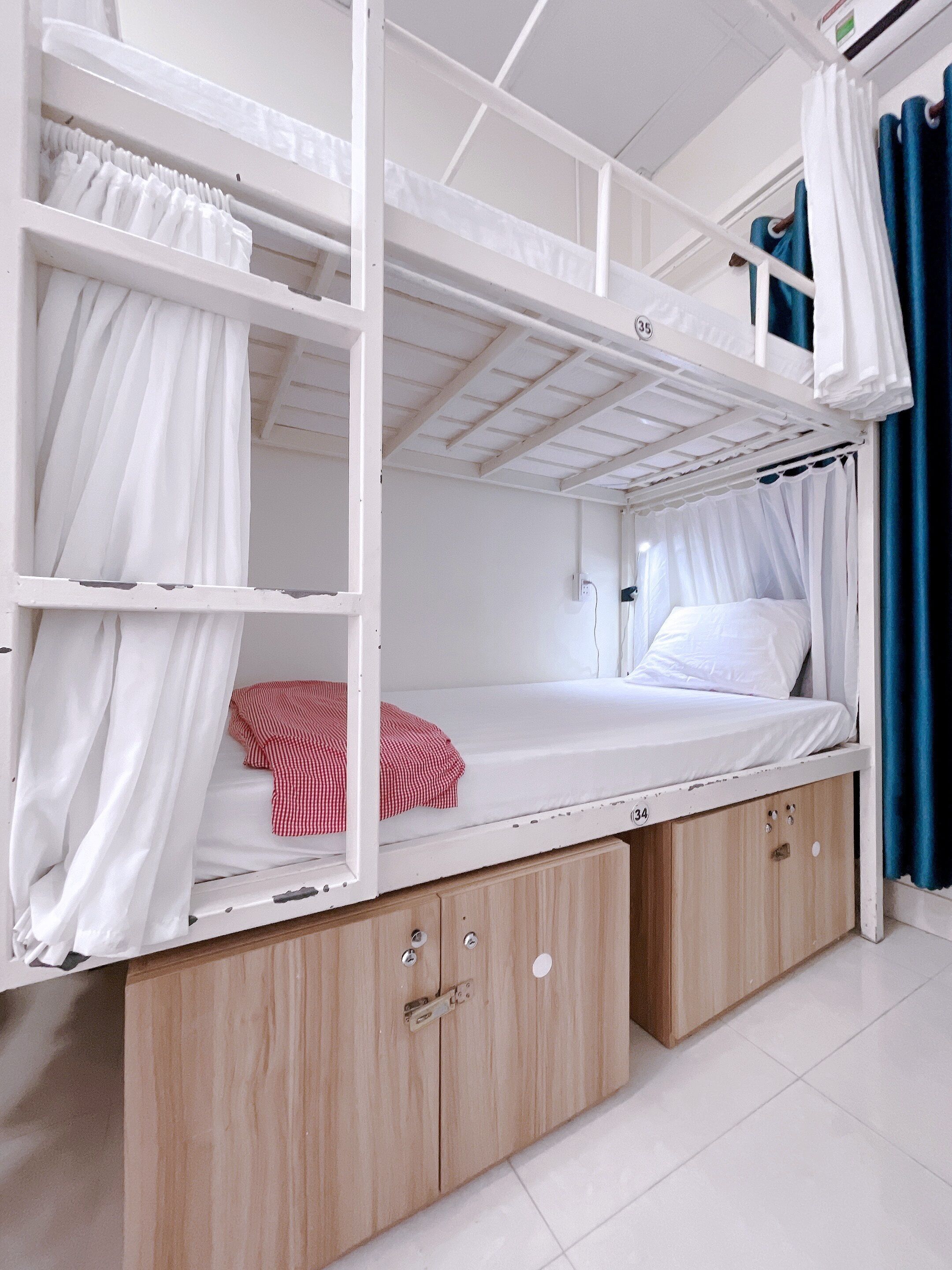 A bunk bed with a lower bunk, a wooden cabinet below, and a curtain on the upper bunk.