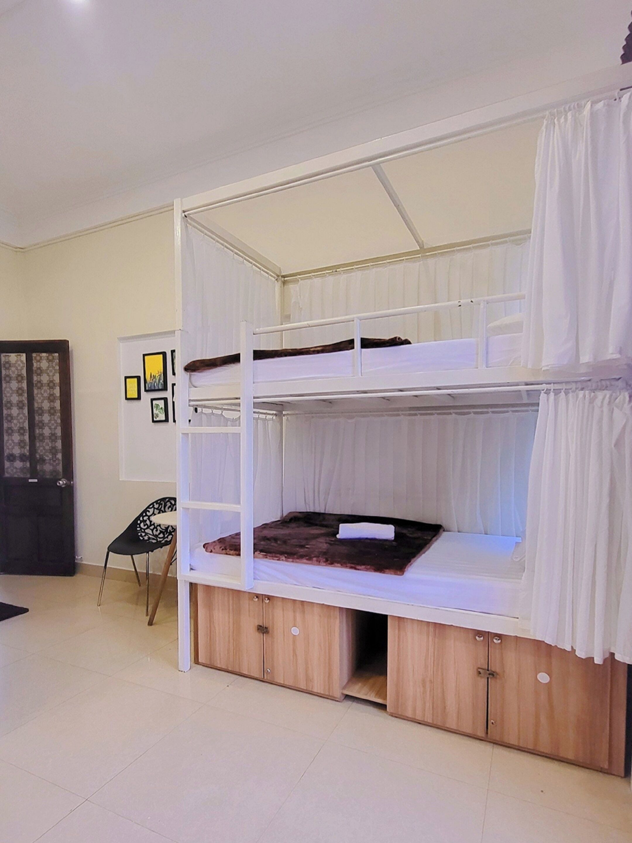 Una cama individual con estructura de madera y ropa de cama blanca, una silla y cuadros en la pared.