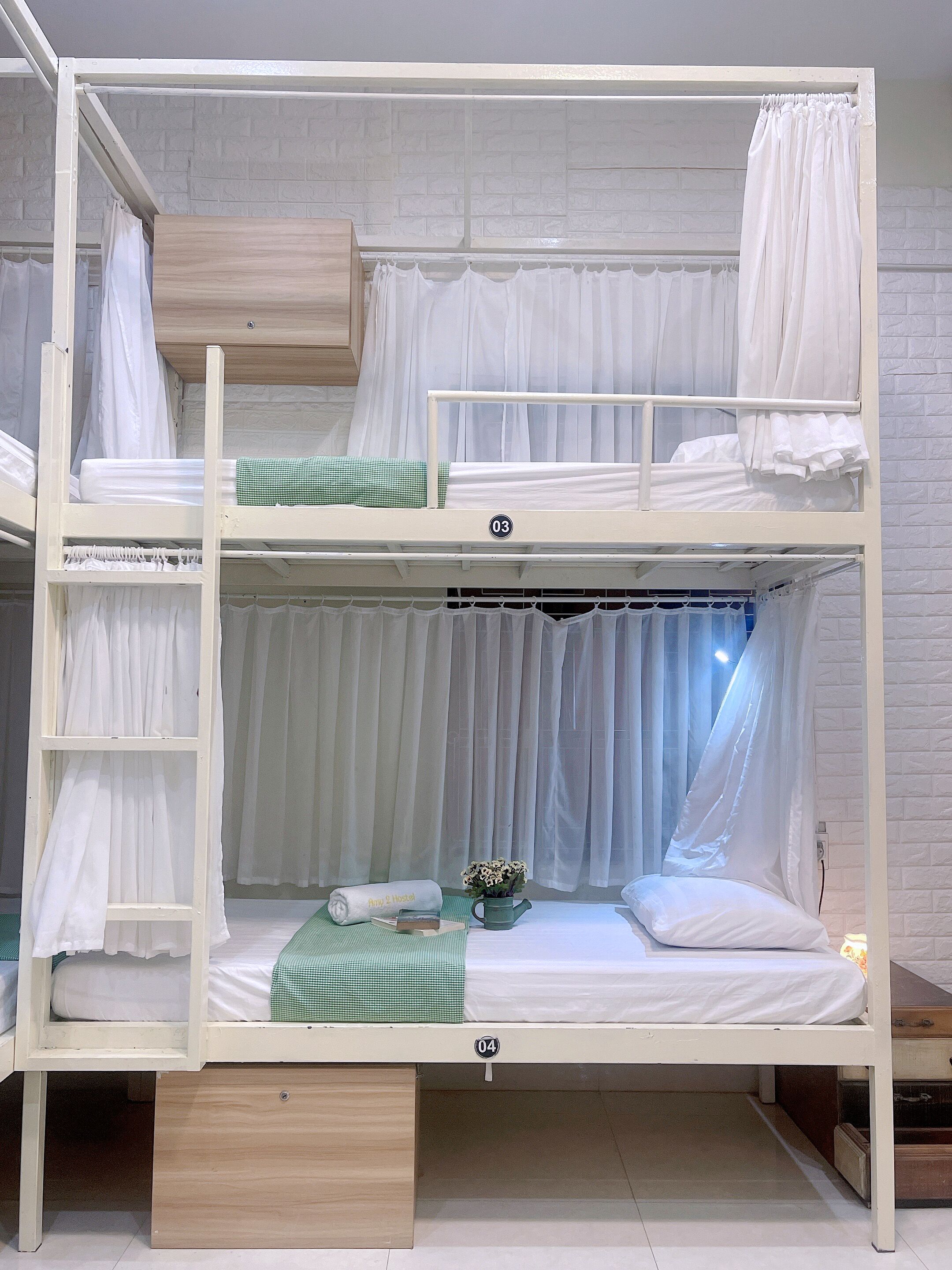 A bunk bed with two levels, each with a mattress and pillows. There is a ladder on the left side, and a small table with a flower vase and a book on the lower bunk.