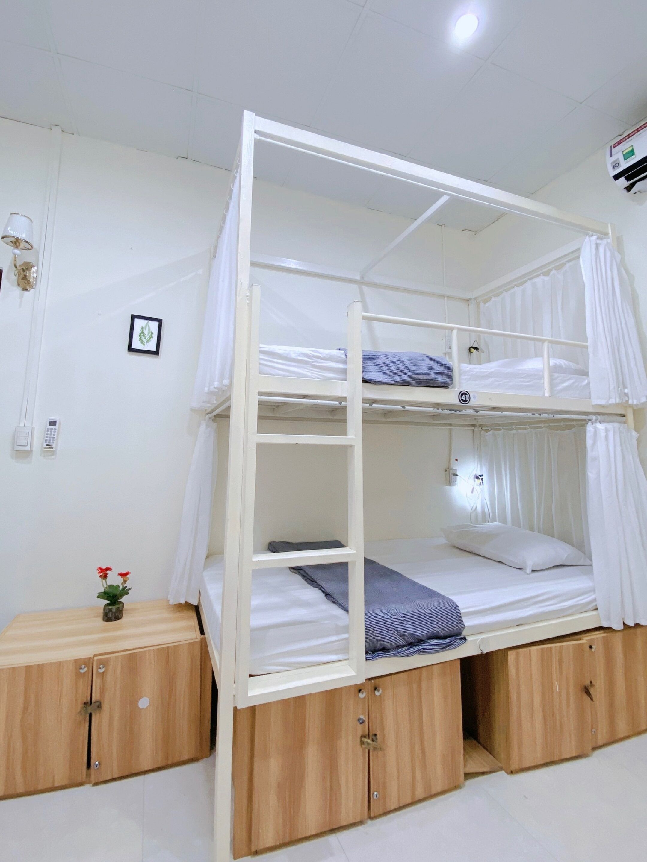 A bunk bed with a canopy, wooden storage cabinets, and a small bedside table with a vase of flowers.