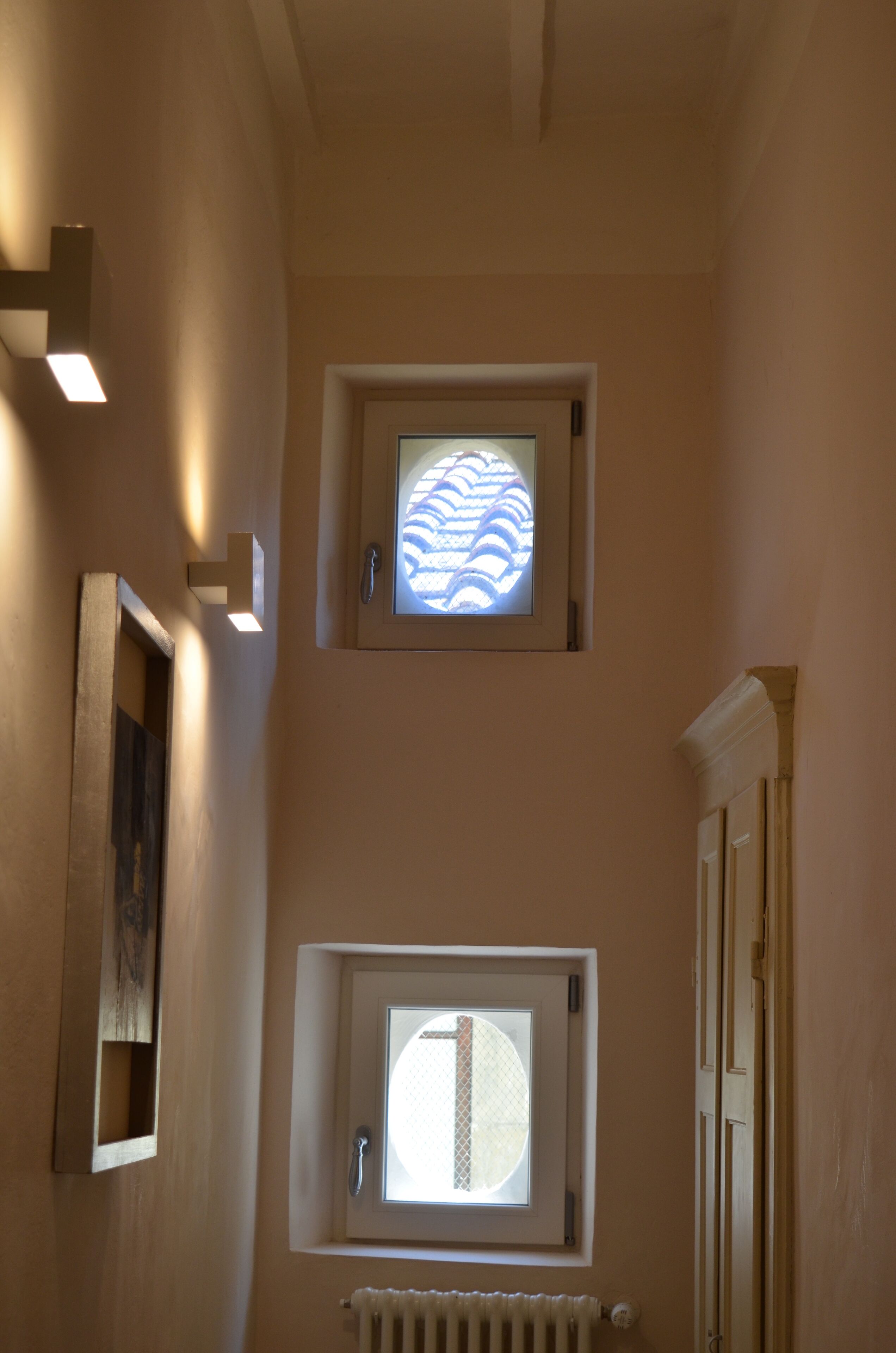 A hallway with two windows, one with a patterned glass and another with a plain glass. There is a radiator below the plain glass window.