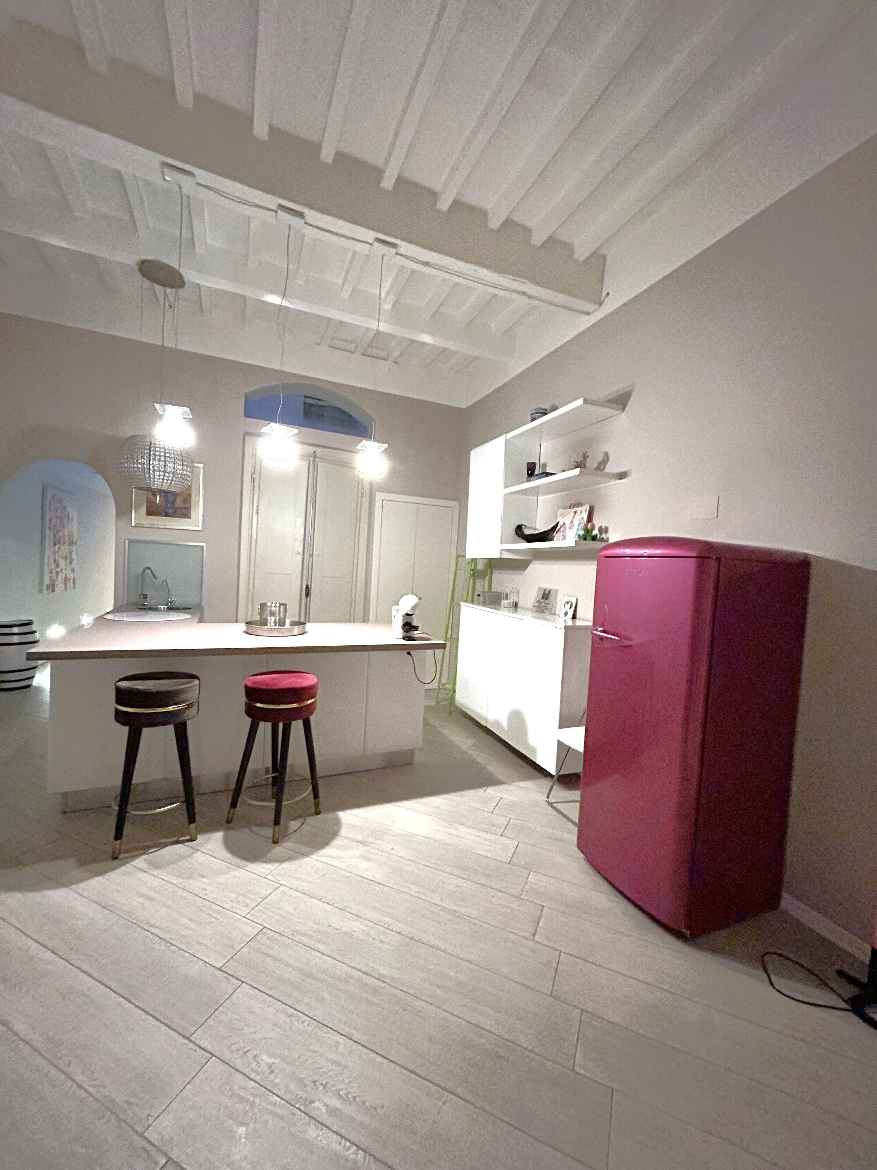 A kitchen with a white countertop, two stools, a pink refrigerator, and a white cabinet.