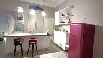 A kitchen with a white countertop, two stools, a pink refrigerator, and a white cabinet.